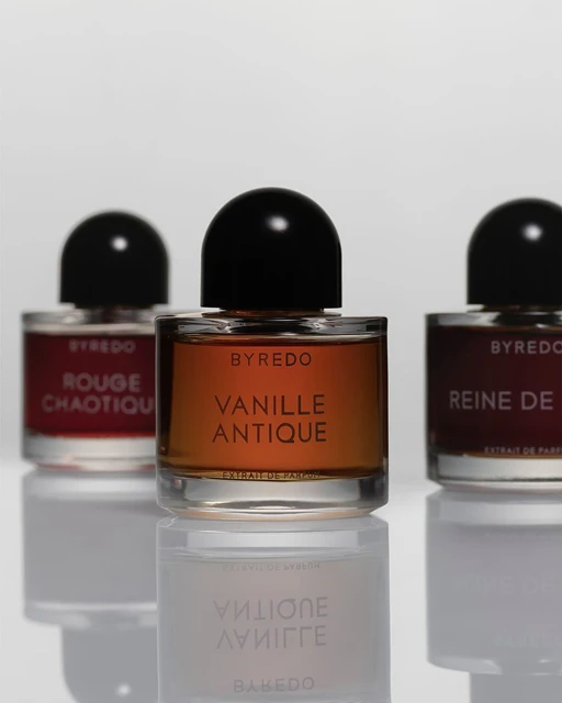 Three Byredo perfume bottles are displayed on a reflective white surface, with the center bottle in focus highlighting 'Vanille Antique'.