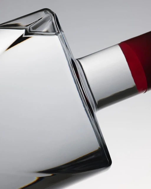 Close-up studio shot of a clear glass bottle with a red band at the neck against a neutral gradient backdrop, showcasing a beverage.