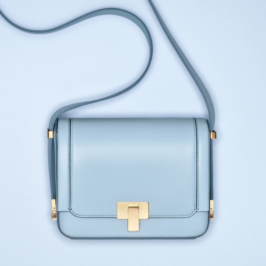Light blue leather crossbody bag with gold hardware on a light blue background. Stylish fashion accessory for women. Studio shot, product photography.