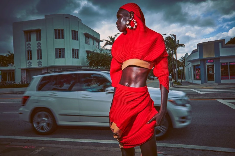 Fashionable Black woman in red outfit posing on a city street with vintage buildings and a passing car in Miami, Florida.