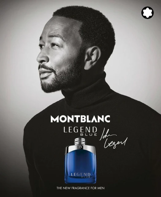 Montblanc fragrance ad featuring John Legend in black turtleneck with a bottle of Legend Blue, set against a light grey backdrop.