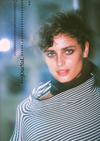 Close-up studio shot of a young woman with dark hair and light eyes, wearing a striped poncho and a black top.