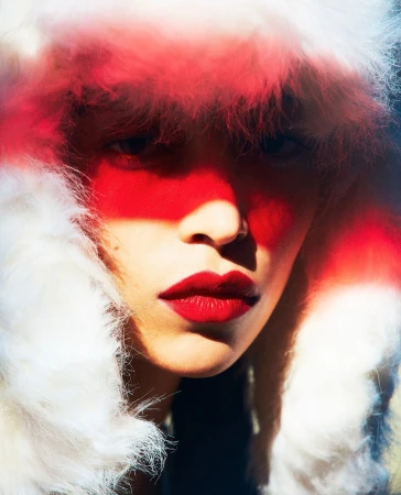 Close-up portrait of a woman wearing a white fluffy faux fur ushanka hat with striking red makeup and dark lipstick.