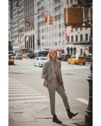 Model in a grey pinstripe suit standing on a New York City street with traffic and American flags.