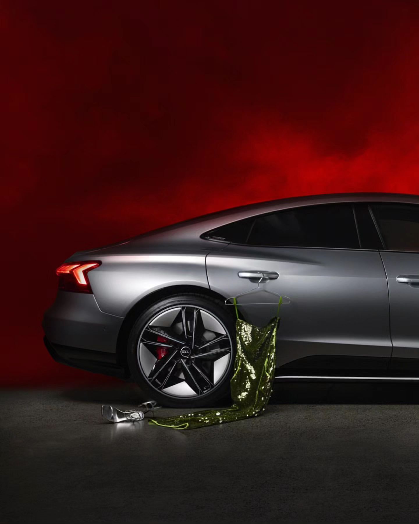 Silver Audi e-tron GT on display with a green sequin dress and clear heels against a red backdrop in a fashion and automotive shoot.