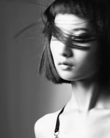 Close-up portrait of a woman with dark hair blowing across her face in black and white by photographer Guy Coombes.