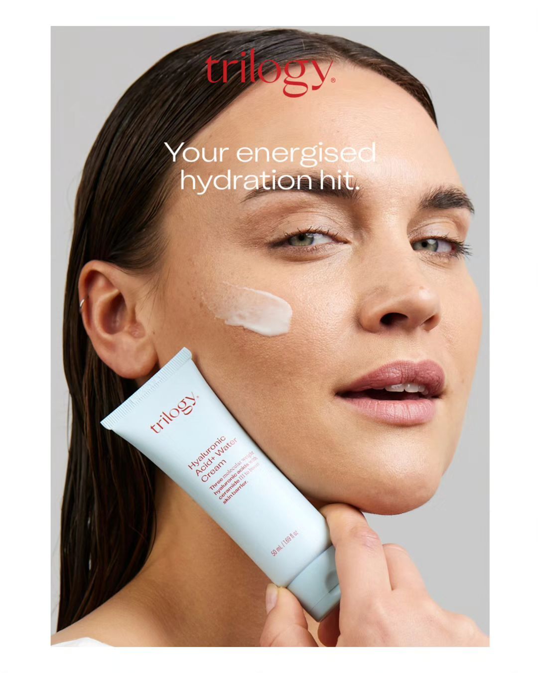 A woman applies Trilogy Hyaluronic Acid+ Water Cream to her face in a close-up shot, promoting skincare and beauty.