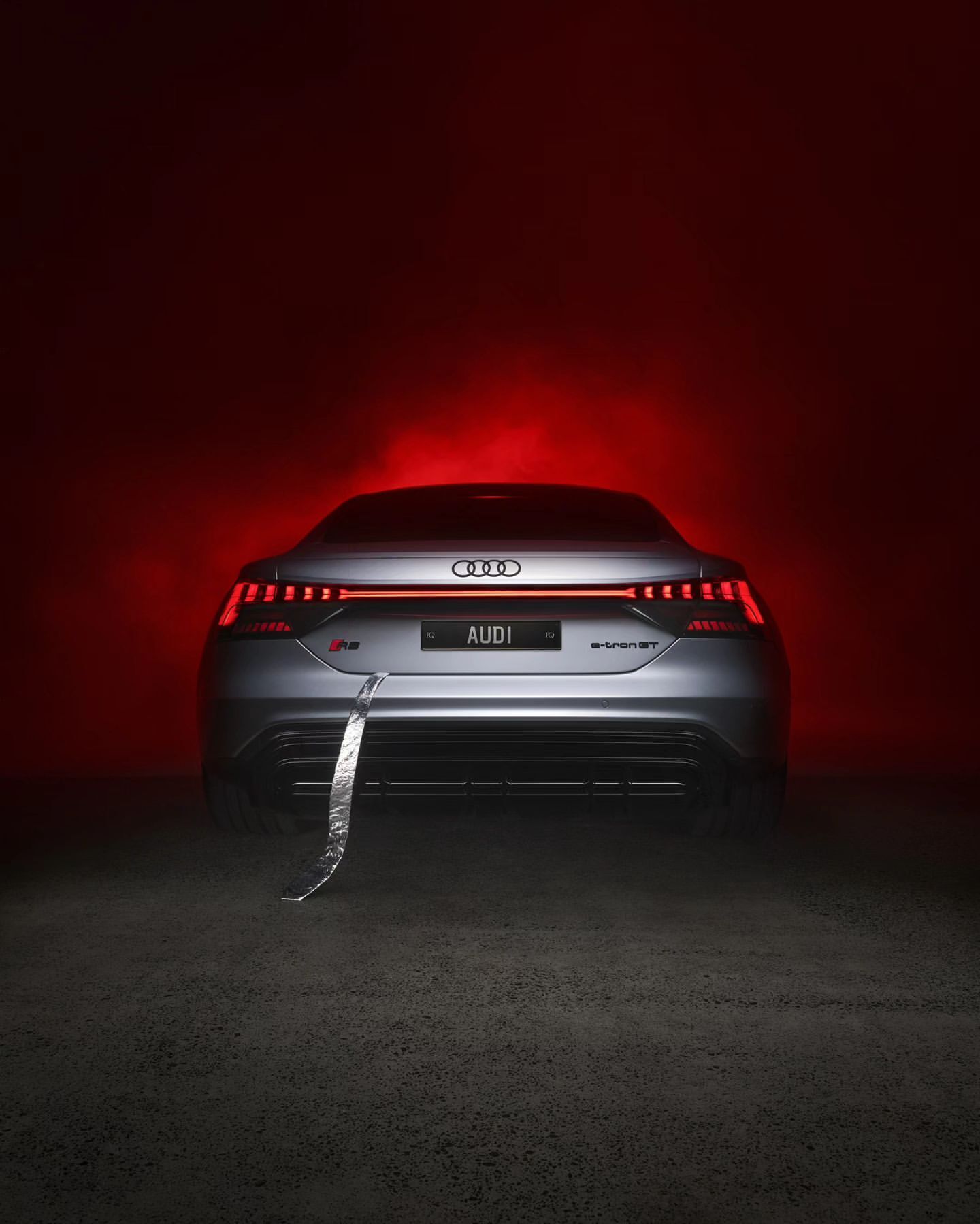Sleek gray Audi e-tron GT in a studio, bathed in vivid red lighting, emphasizing its modern design and dynamic lines, and high-tech aesthetics.