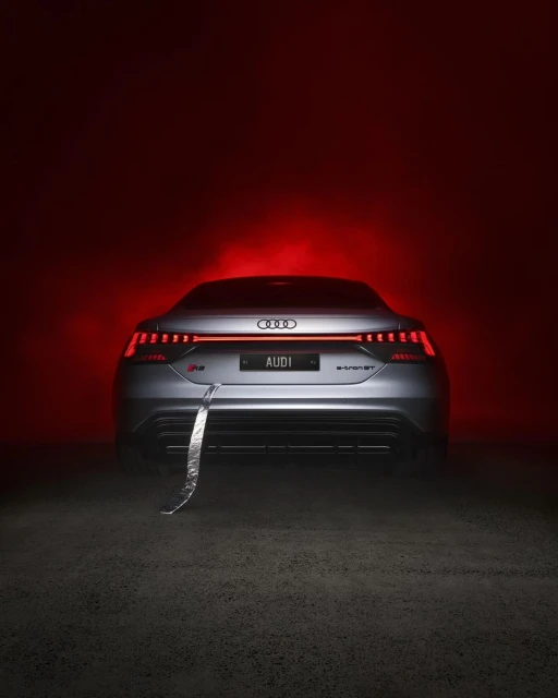 Sleek gray Audi e-tron GT in a studio, bathed in vivid red lighting, emphasizing its modern design and dynamic lines, and high-tech aesthetics.
