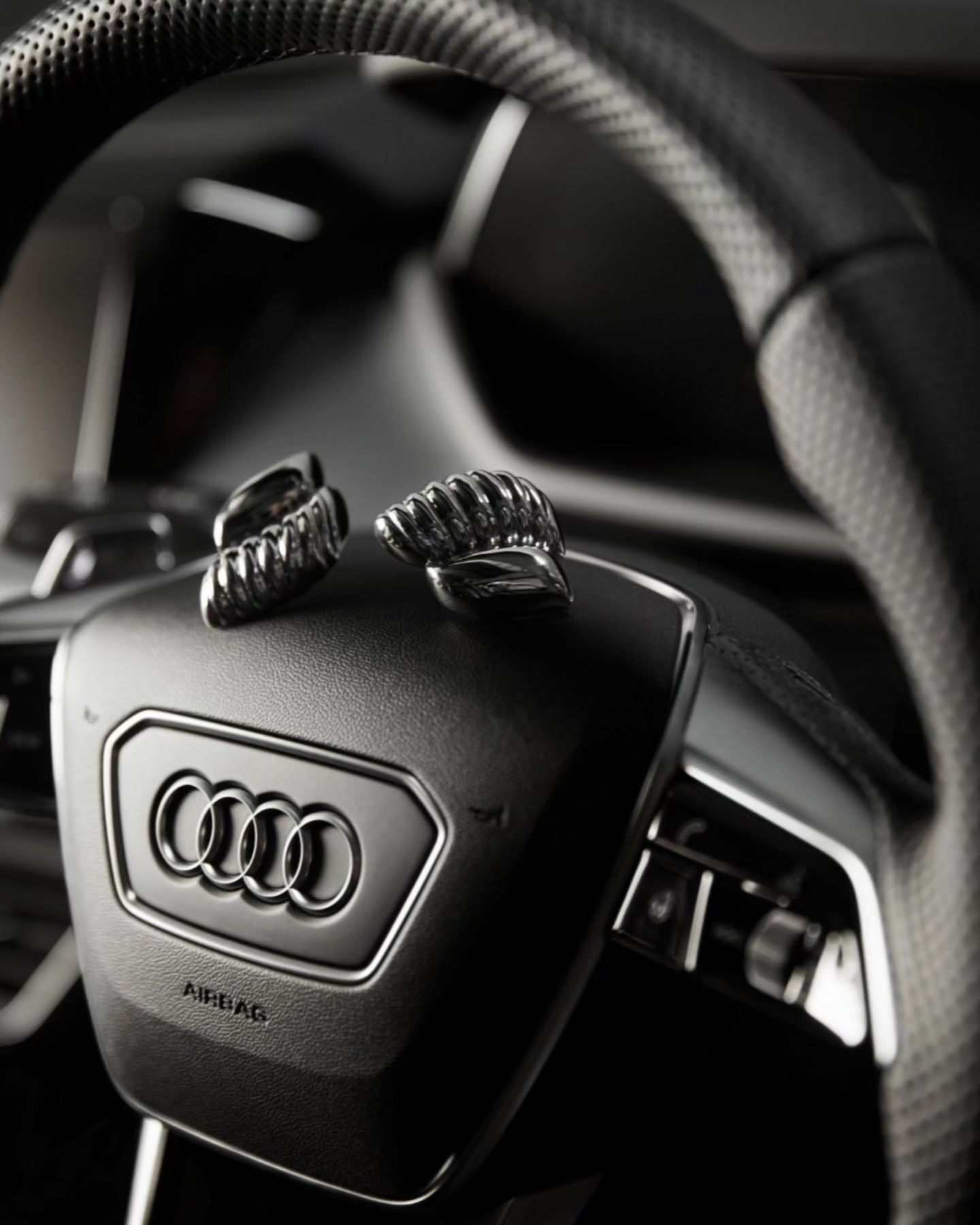 Close-up of a black Audi steering wheel with the brand logo and pair of silver cufflinks on it in a car interior.