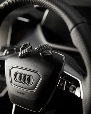 Close-up of a black Audi steering wheel with the brand logo and pair of silver cufflinks on it in a car interior.
