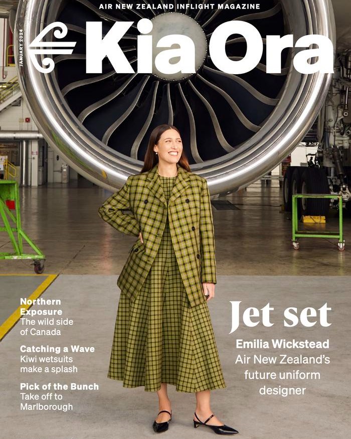 Magazine cover featuring a smiling woman in a green plaid dress and blazer, standing in front of an airplane engine inside a hangar.