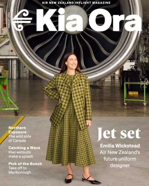 Magazine cover featuring a smiling woman in a green plaid dress and blazer, standing in front of an airplane engine inside a hangar.