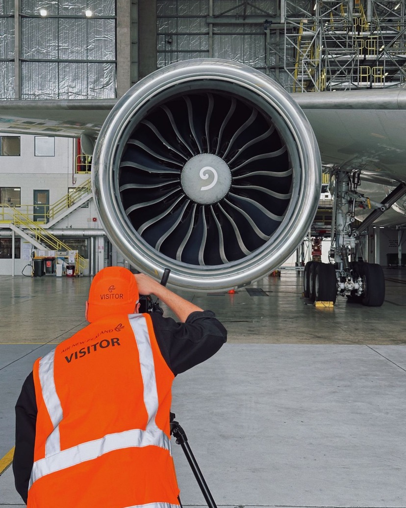 Close-up of a jet engine with a person in a safety vest taking a picture of it in a hangar.