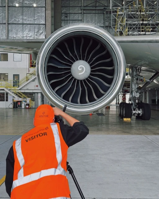 Close-up of a jet engine with a person in a safety vest taking a picture of it in a hangar.