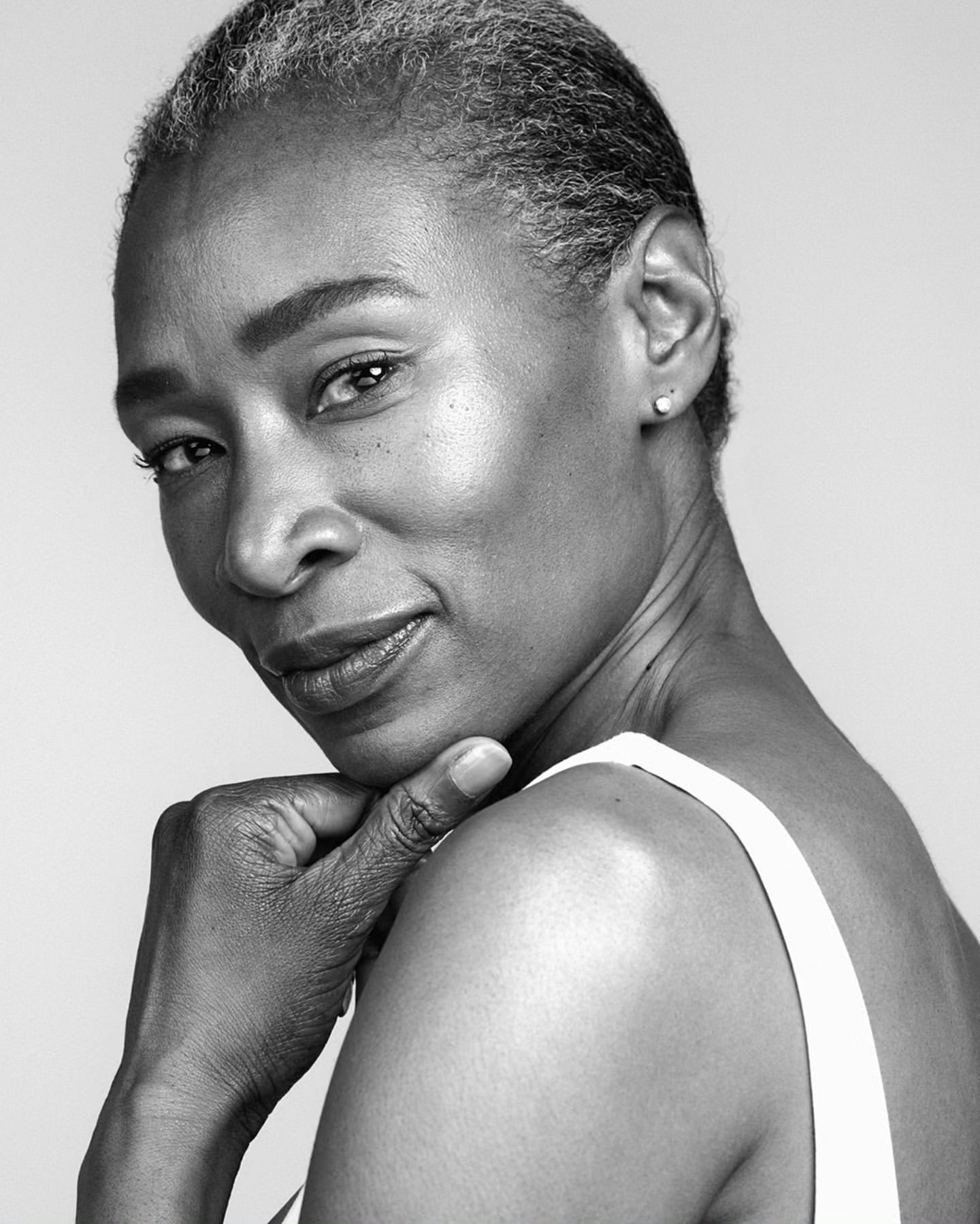 Black and white portrait of a mature Black woman with short gray hair, wearing a white top and posing with her hand to her chin.