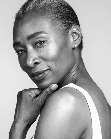Black and white portrait of a mature Black woman with short gray hair, wearing a white top and posing with her hand to her chin.
