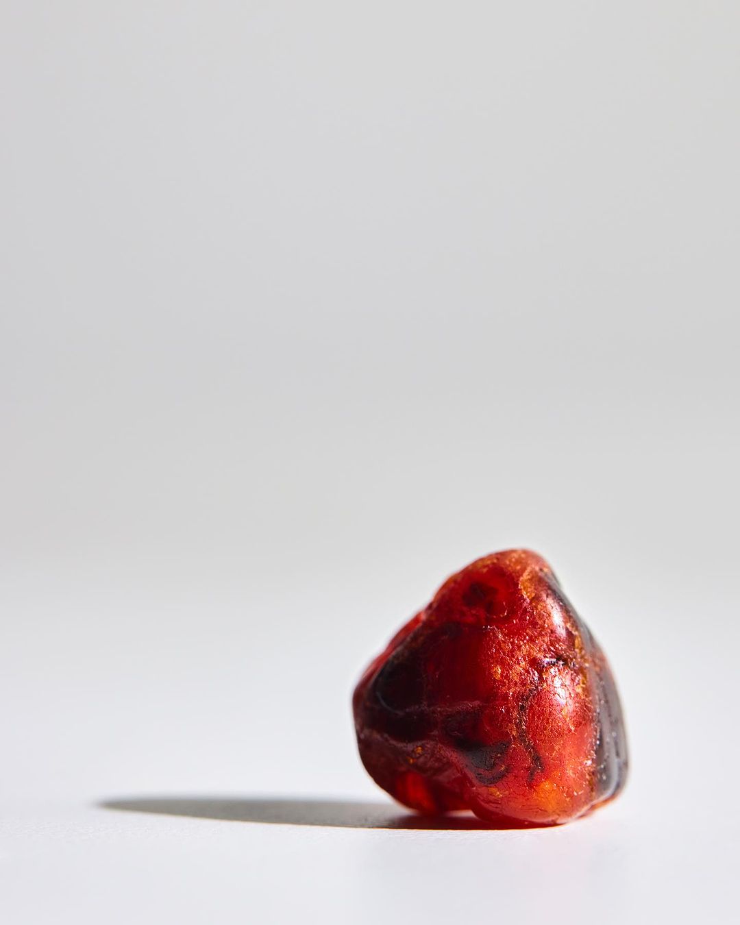 Close-up studio shot of a translucent red amber stone on a white surface with a shadow, showcasing its texture and color.