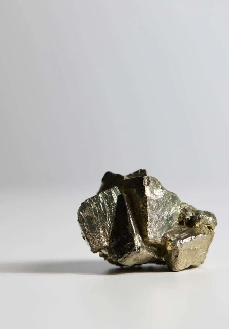 Detailed studio shot of a pyrite mineral specimen featuring metallic luster and crystalline structure against a gradient background.
