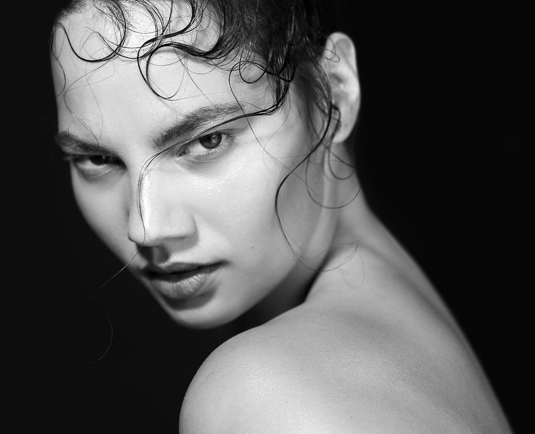Striking black and white portrait of a woman with wet hair, looking intensely at the camera against a dark background, emphasizing natural beauty.