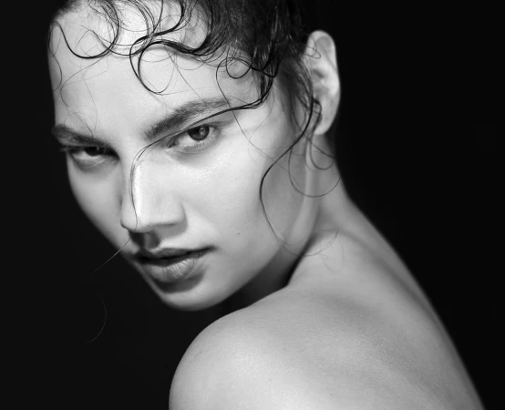 Striking black and white portrait of a woman with wet hair, looking intensely at the camera against a dark background, emphasizing natural beauty.