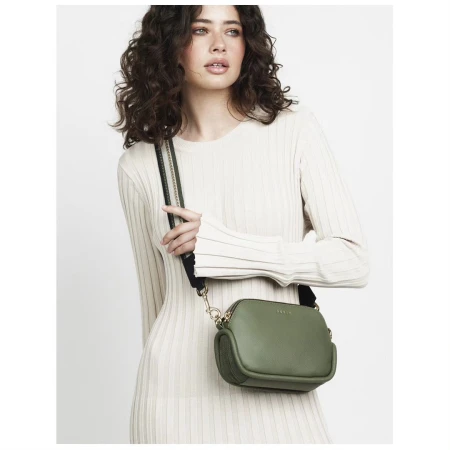 Woman wearing a light colored ribbed dress and holding a small olive green cross body bag with a black shoulder strap.