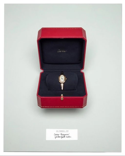 Close-up of a gold wristwatch displayed in its original red box with navy blue lining on a white background. Watch faces up.