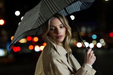 Woman holding a patterned umbrella in a night street with blurred colorful bokeh lights in Auckland by Guy Coombes