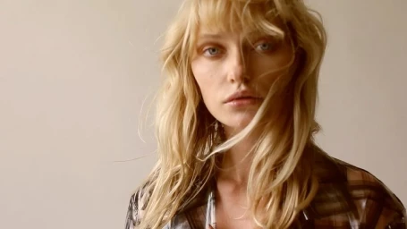Portrait of a blonde woman with fringe wearing a patterned top against a neutral light background