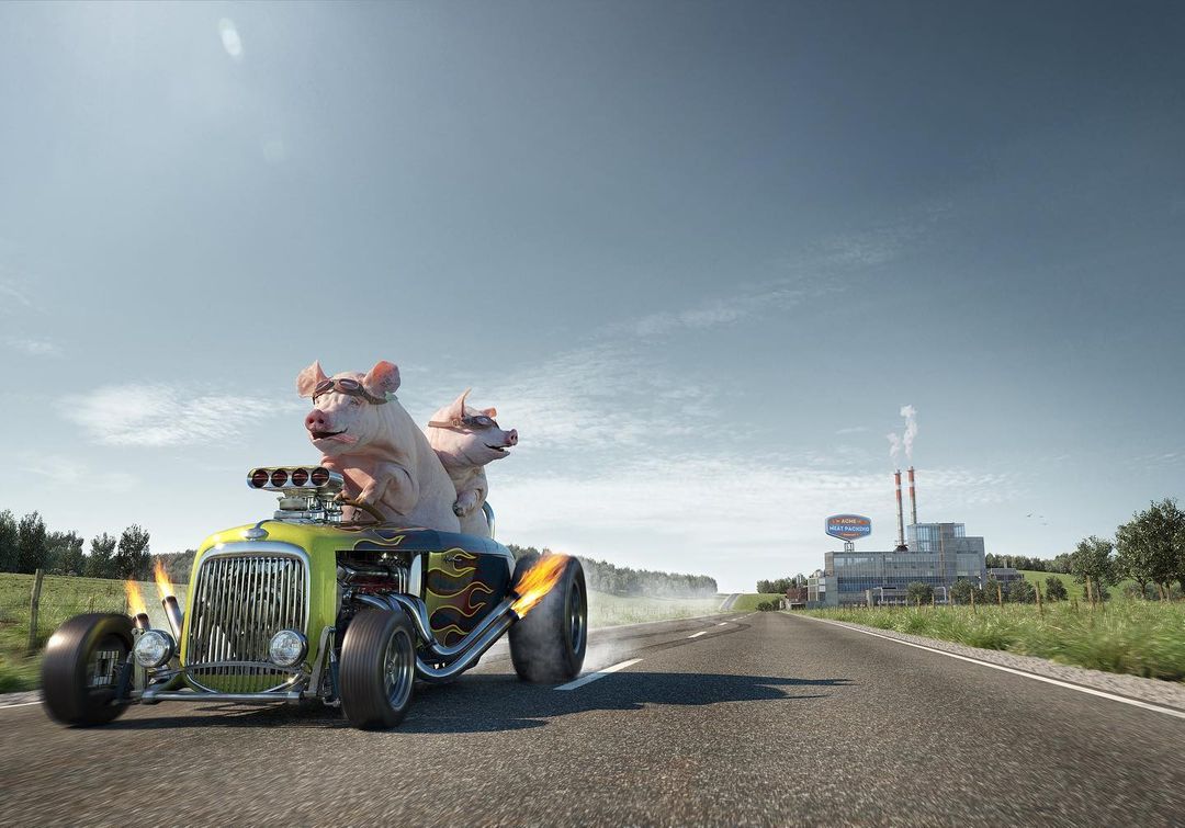 Two pigs wearing goggles drive a hot rod car with flames on the side down a road with a factory in the background on a sunny day.