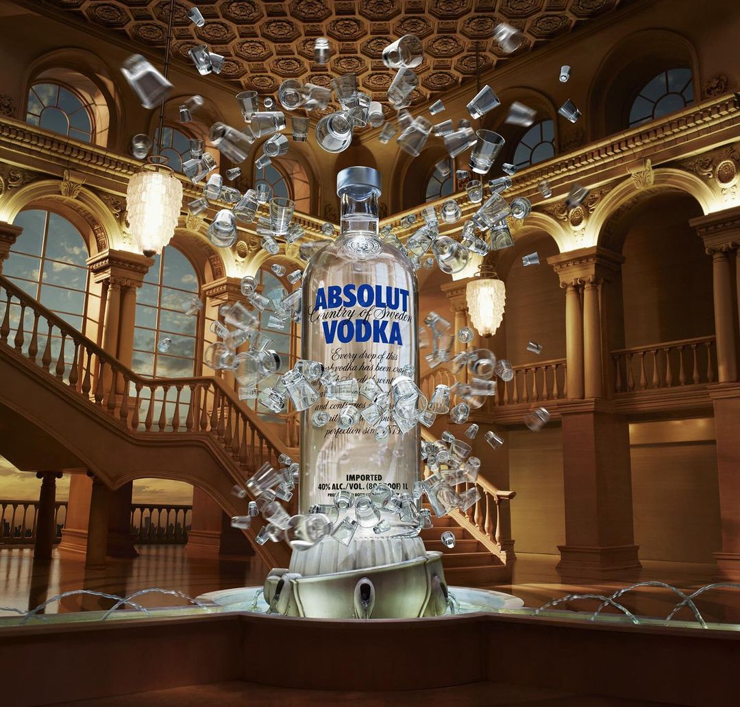 Absolut Vodka bottle with ice in a grand hall, surrounded by floating ice cubes and small glasses, lit by chandeliers.
