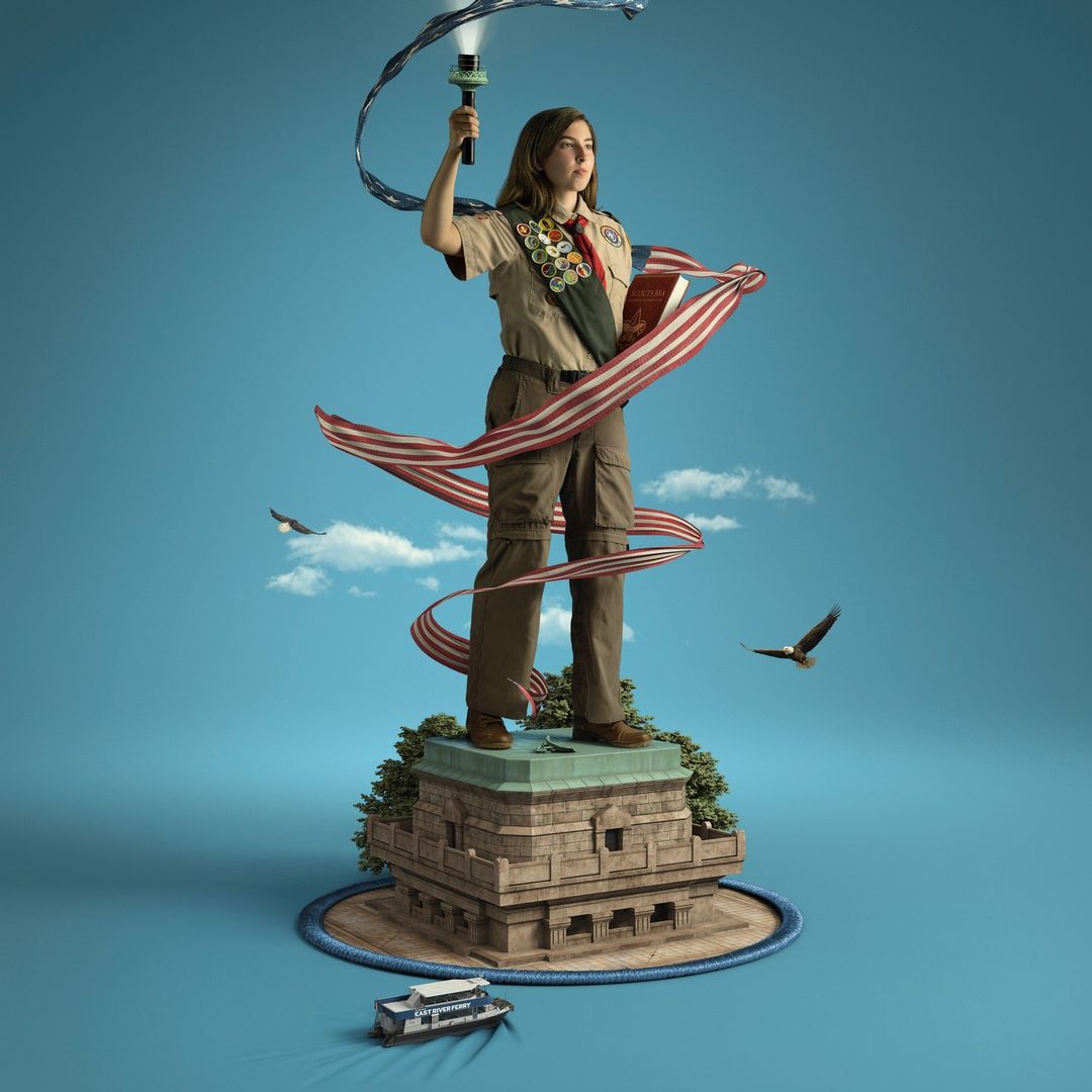 Young person in Boy Scout uniform stands atop a miniature Statue of Liberty, holding a torch with ribbon in a digitally enhanced image.