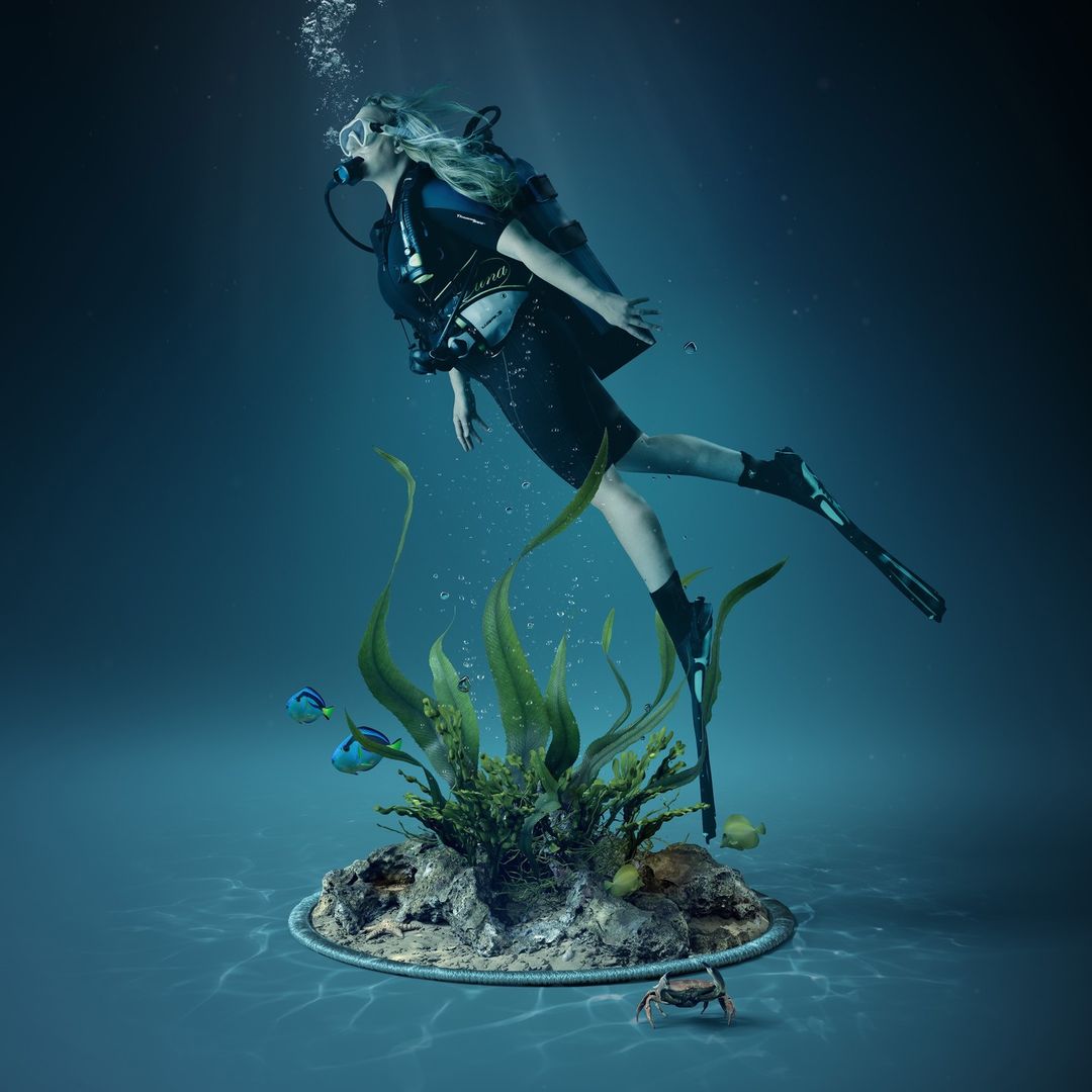 Woman in scuba gear swims underwater near coral reef, surrounded by bubbles and aquatic life in blue-toned environment.