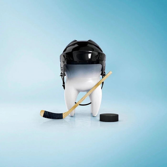 A stylized white molar tooth wearing a black hockey helmet with a hockey stick and puck against a blue gradient studio backdrop.