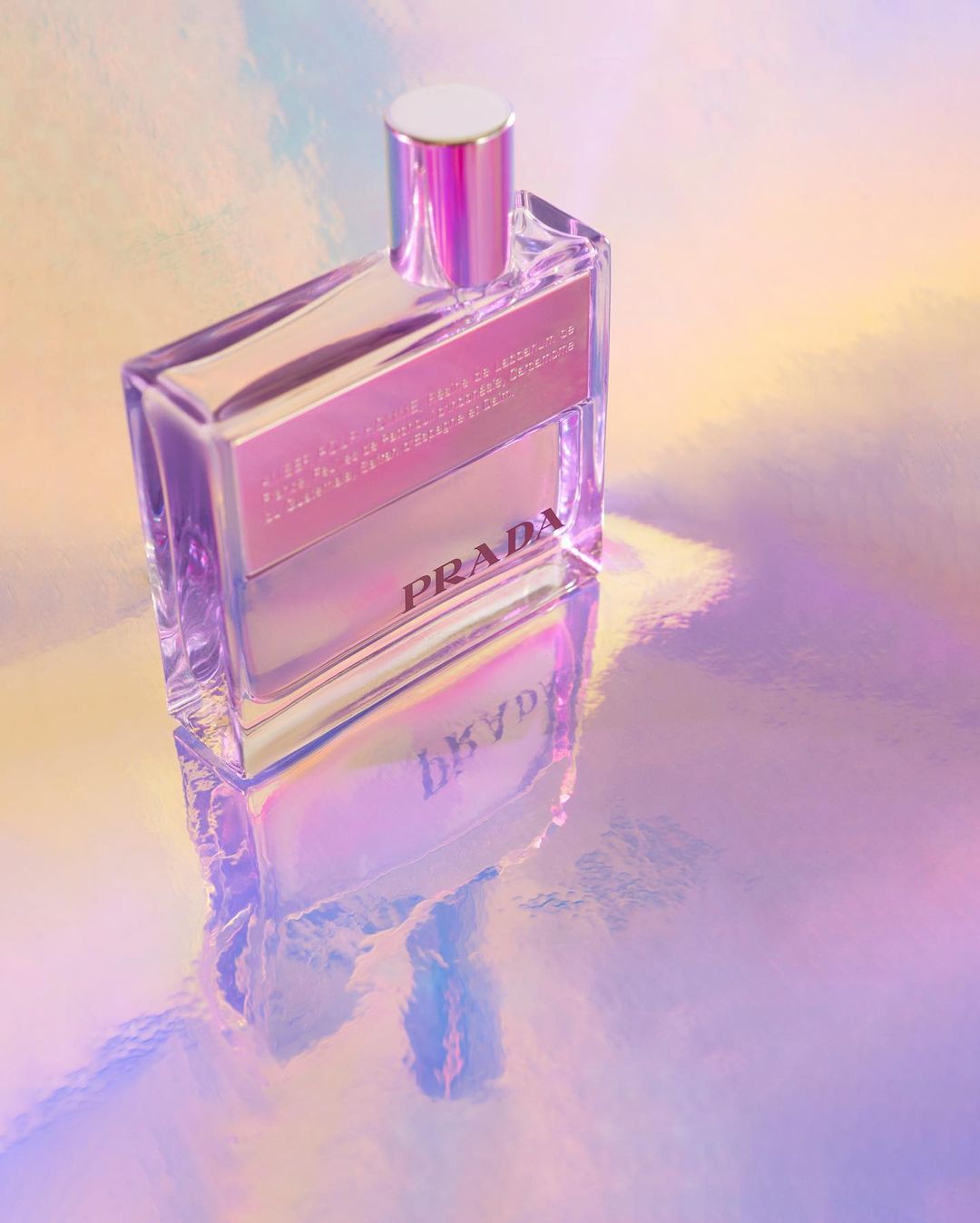 Prada perfume bottle on iridescent surface. Minimalist product shot showcases the fragrance's sleek design and vibrant, reflective backdrop.