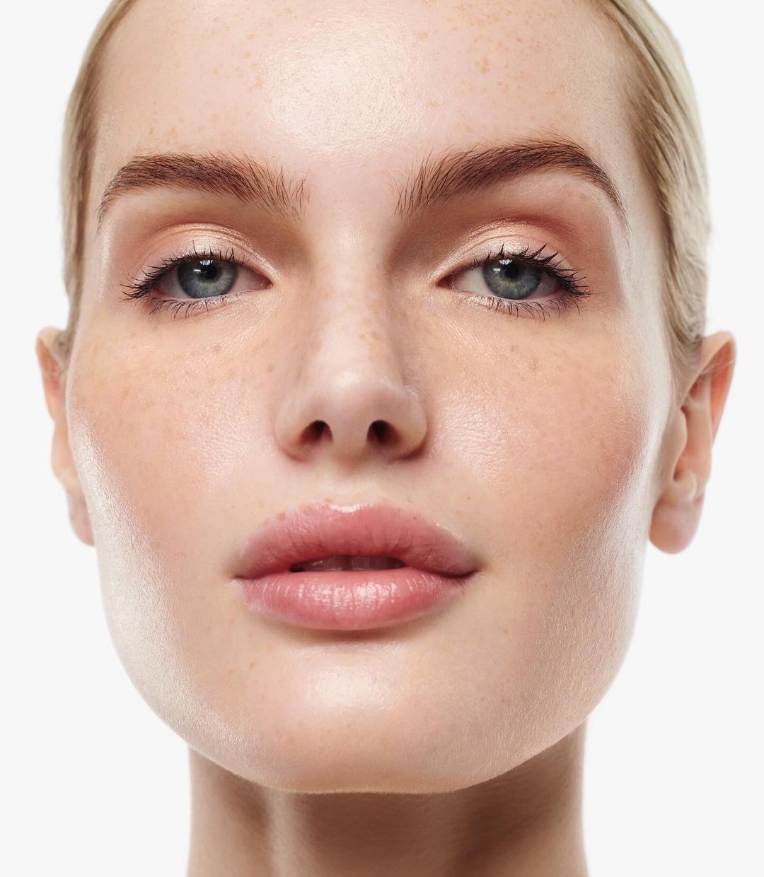 Close-up portrait of a blonde woman with fair skin, blue eyes, and freckles, set against a stark white background.