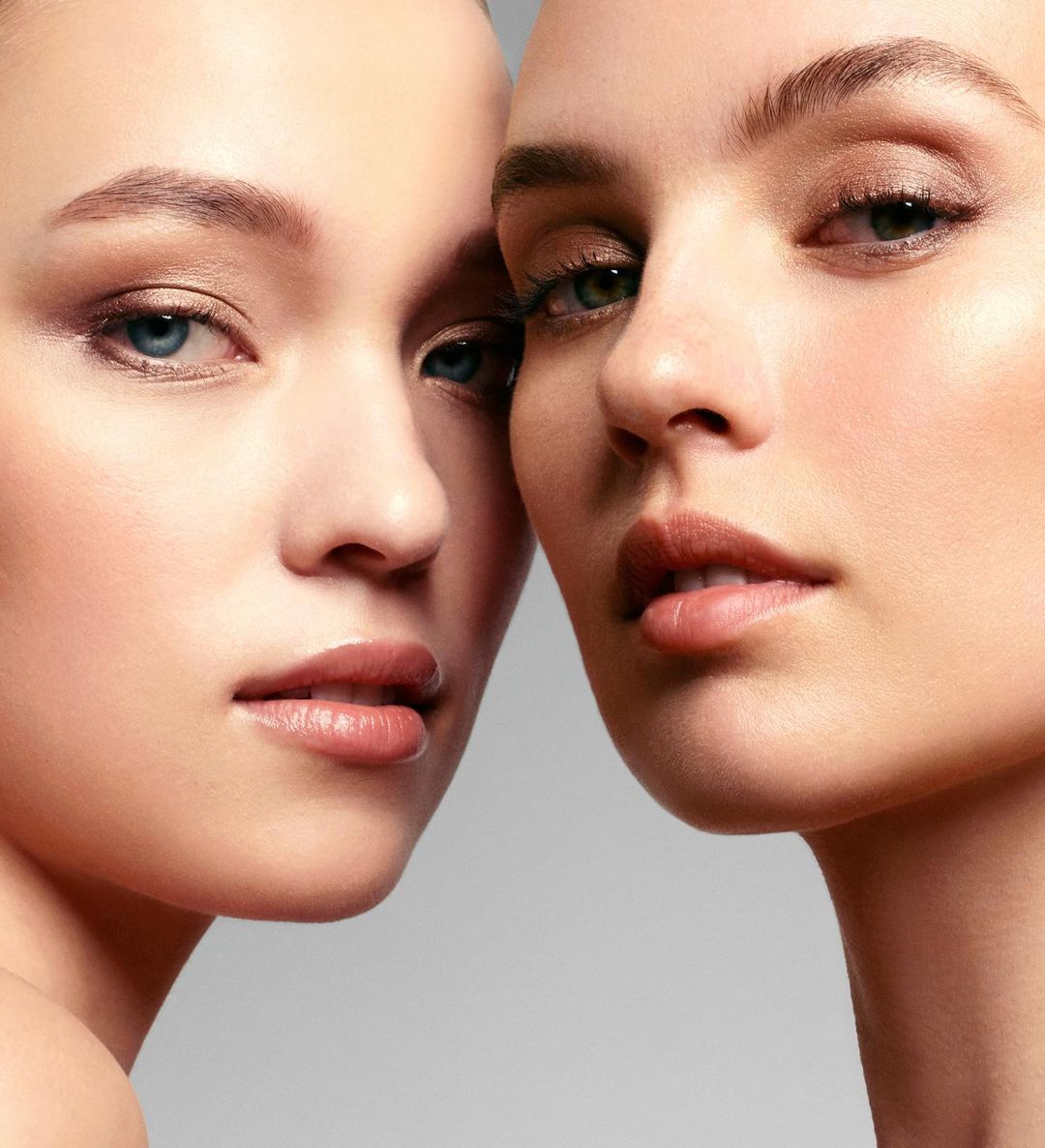 Close-up shot of two young fair-skinned women with neutral makeup and soft lighting highlighting their features in a beauty editorial.