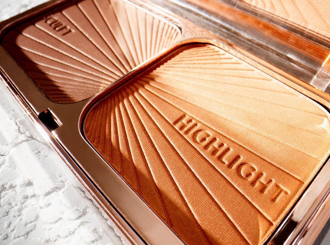 Close-up of an open bronze-toned makeup compact, highlighting both a contour shade and a highlighter, emphasizing the ray pattern design.
