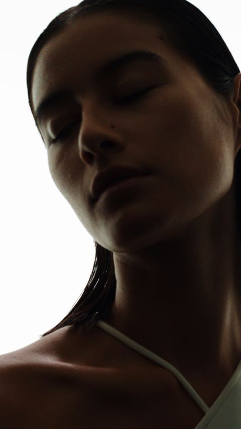 Close up portrait of a woman with wet slicked back hair and closed eyes against a bright white background