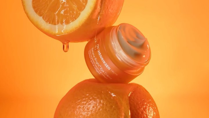 Cosmetic product jar with oranges against an orange backdrop. Close-up shot showcases a product advertisement and vibrant color contrast.