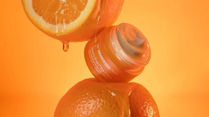 Cosmetic product jar with oranges against an orange backdrop. Close-up shot showcases a product advertisement and vibrant color contrast.
