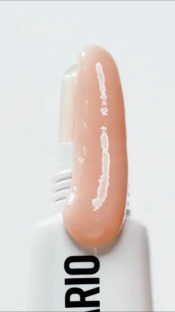 Close-up of beige cosmetic product smear against a white background, showcasing texture, color, and the packaging of the product.