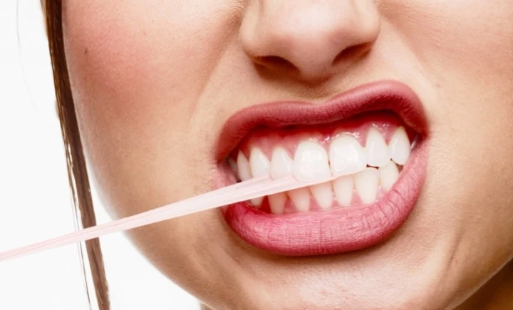 Extreme close-up of a woman's face pulling pink dental floss between her white teeth, showcasing oral care and dental hygiene.