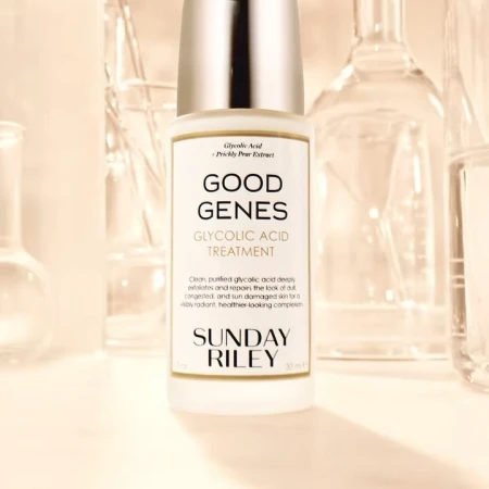 Close-up of Sunday Riley Good Genes Glycolic Acid Treatment bottle with clear lab glassware in background, pale yellow tones.