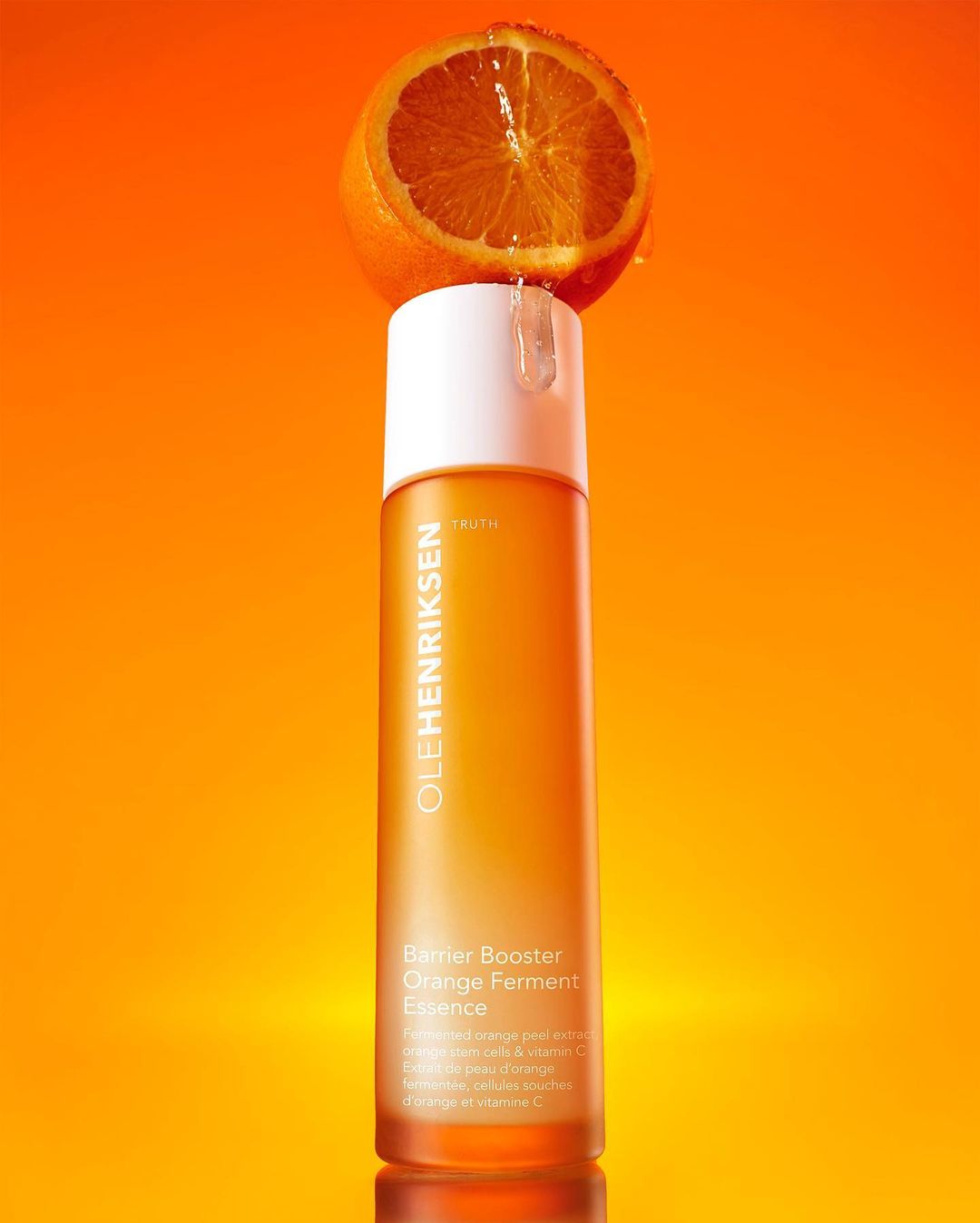 Ole Henriksen Barrier Booster Orange Ferment Essence bottle with half orange on top against an orange gradient background.