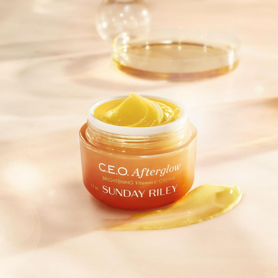 Close-up of Sunday Riley C.E.O. Afterglow Brightening Vitamin C Cream in a jar on a peach-colored surface with soft lighting.