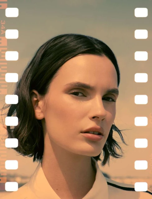 Woman with bob haircut poses indoors with film border. Close-up headshot with neutral expression, warm lighting, and minimalist aesthetic.
