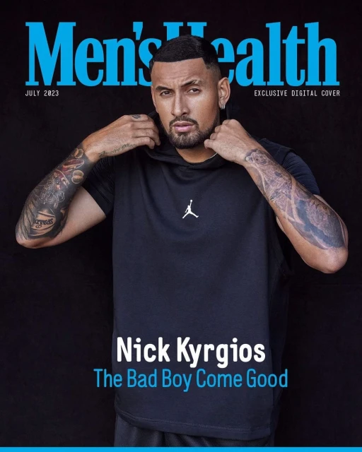 Man in black hoodie posing for Men's Health cover, with tattoos visible on his arms, against a dark background in a portrait shot.