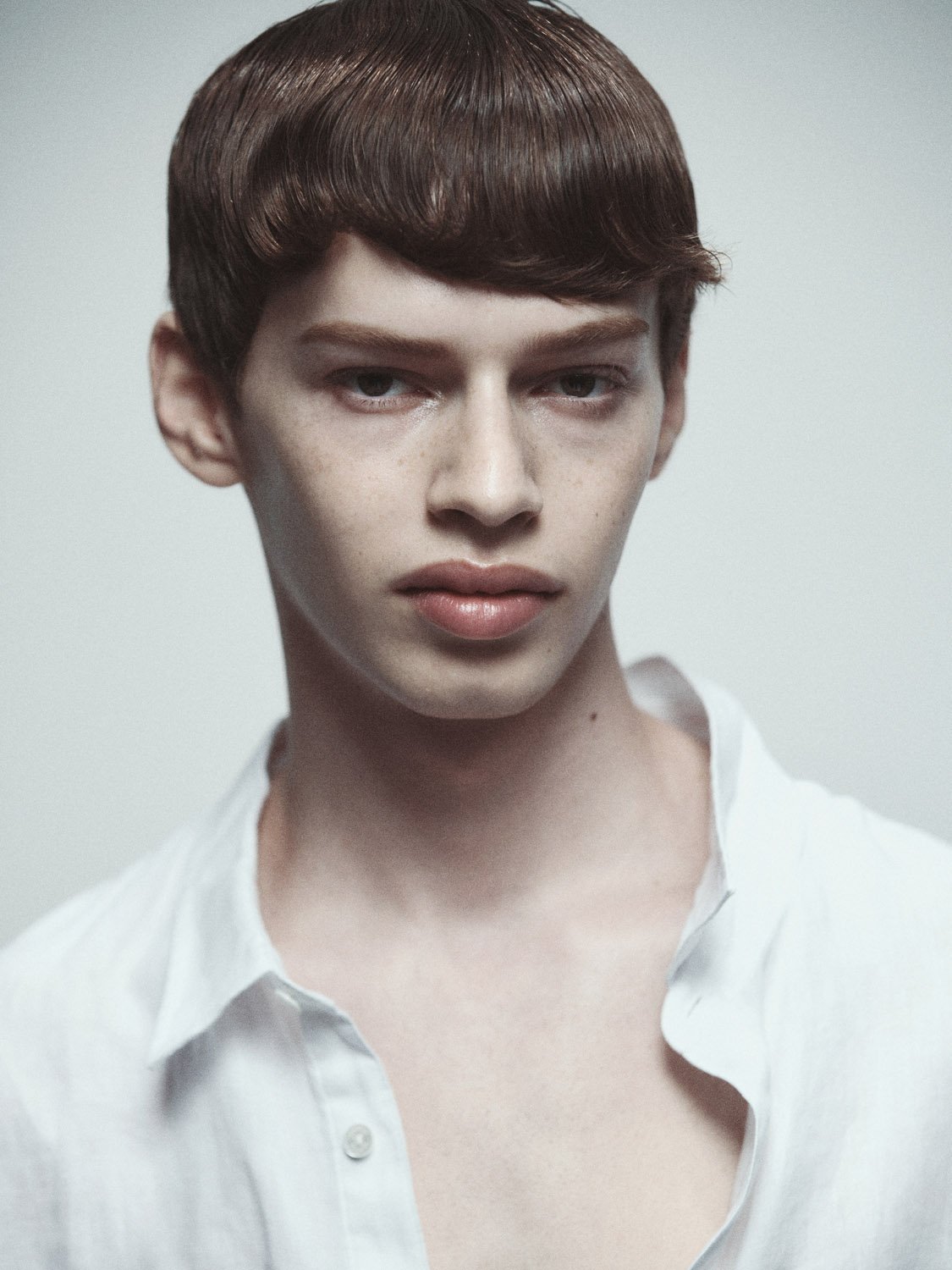 Portrait of a young adult man with dark hair and a white shirt, looking at the camera against a neutral light background.