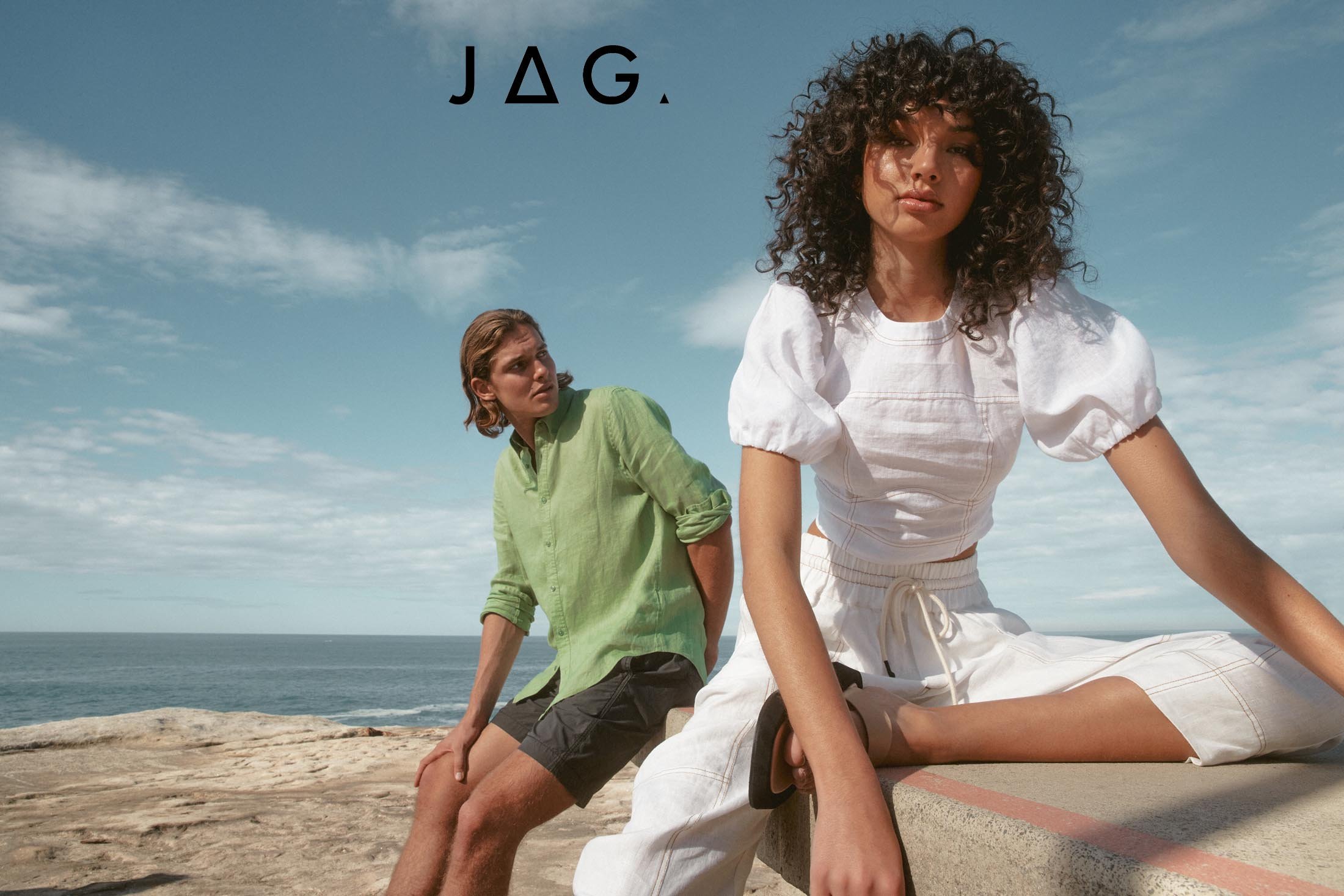 A fashion shot presents a woman in a white top and a man in a green shirt, both on a rocky outcrop with a sunny sky backdrop.